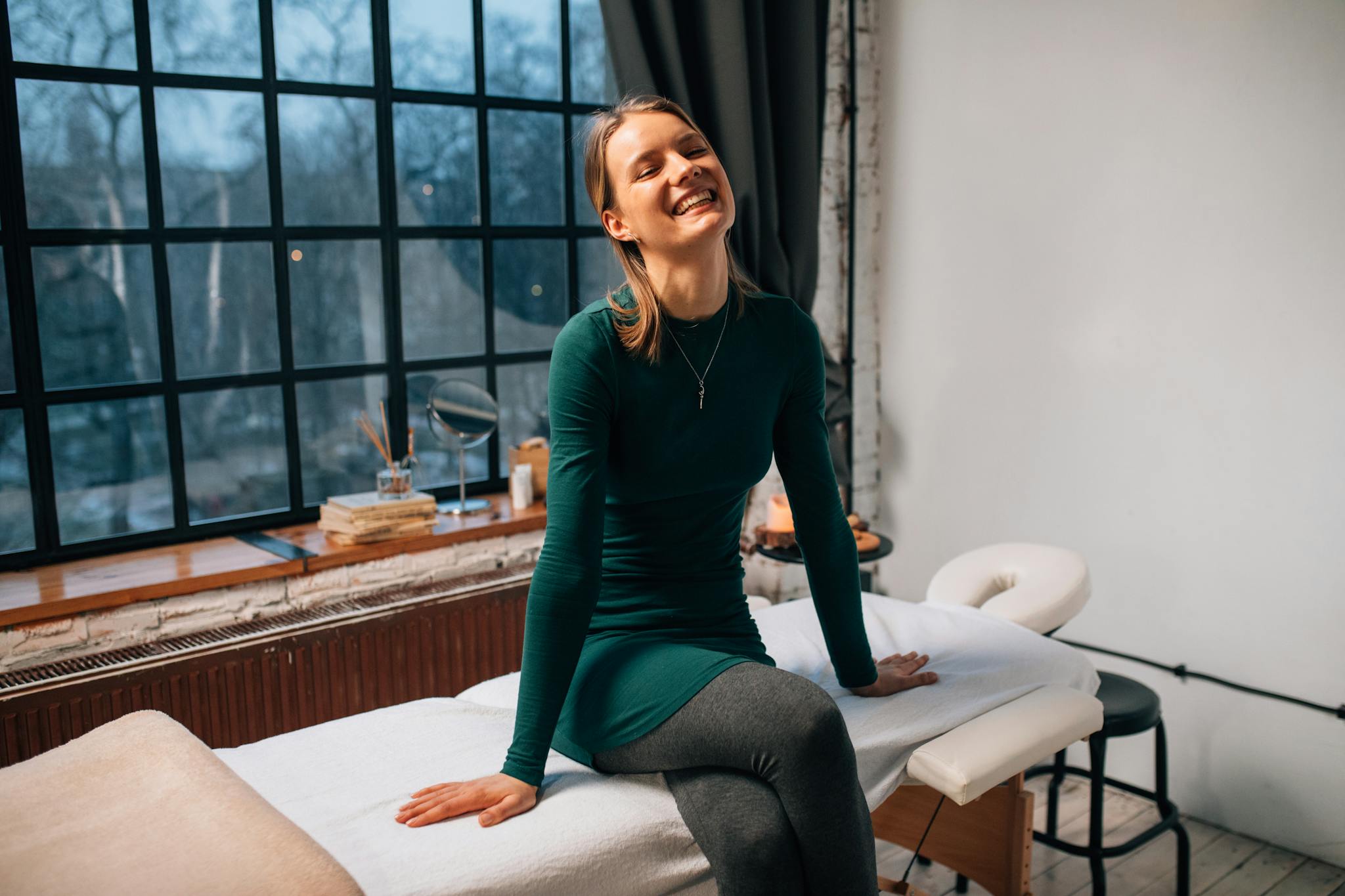 Happy woman sitting on a massage table indoors, enjoying a relaxing spa day.