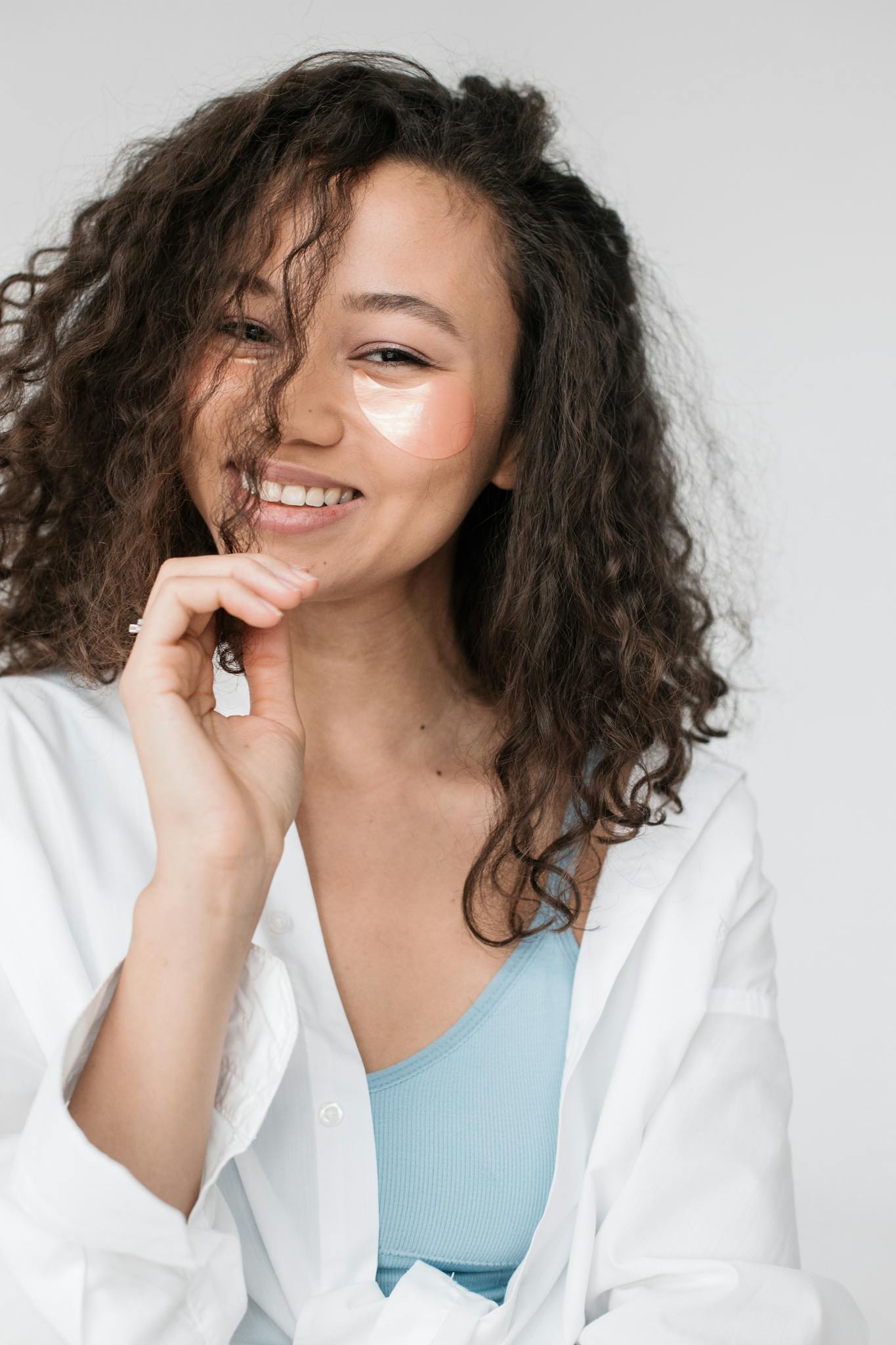 Young woman with curly hair and eye patches smiling confidently in casual attire.